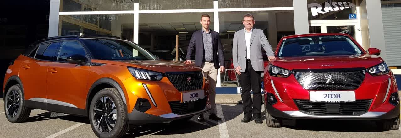 Michael und Dietmar Rasser vor dem Autohaus mit einem orangefarbenen und einem roten Peugeot